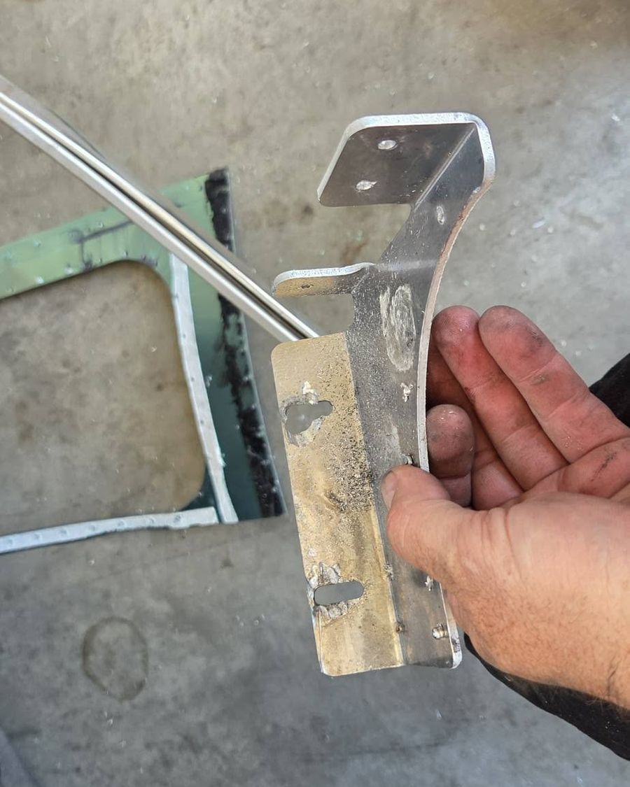 A hand holding a bent metal bracket over a shop floor