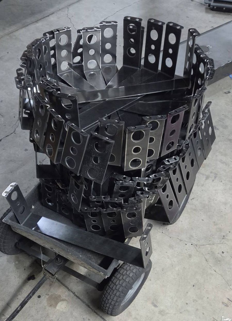 A tall stack of steel brackets on a shop cart
