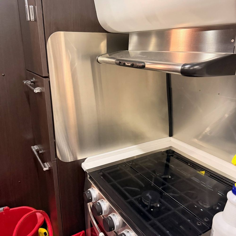 A stainless steel backsplash behind a range hood and stove